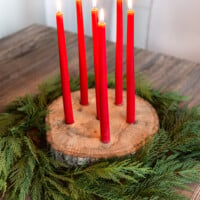 Tree trunk slice taper candle holder for Christmas with cedar branches around it.