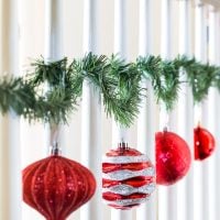 Christmas ornaments hung on staircase spindles with garland ties.