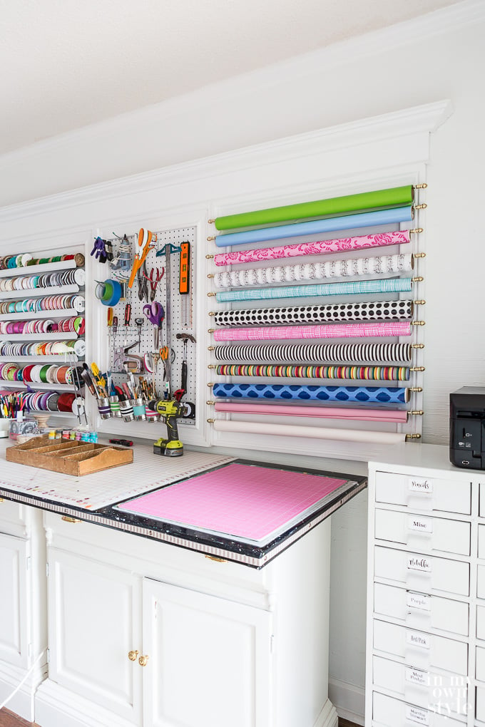 Craft room showing wall with tools, ribbon and gift wrap organized in large white frames.