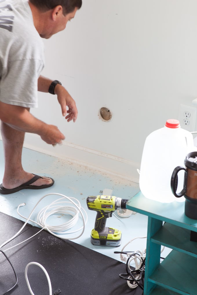 Man working on drilling lower hole in wall for TV cords to run through.