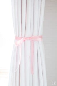 white drape hanging with pink ribbon tied around it to create pleats