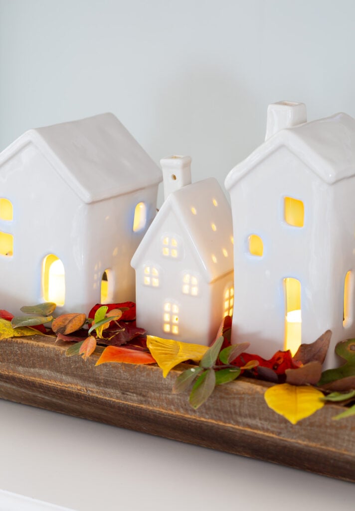 Light up white ceramic village used for fall decoration on a table.