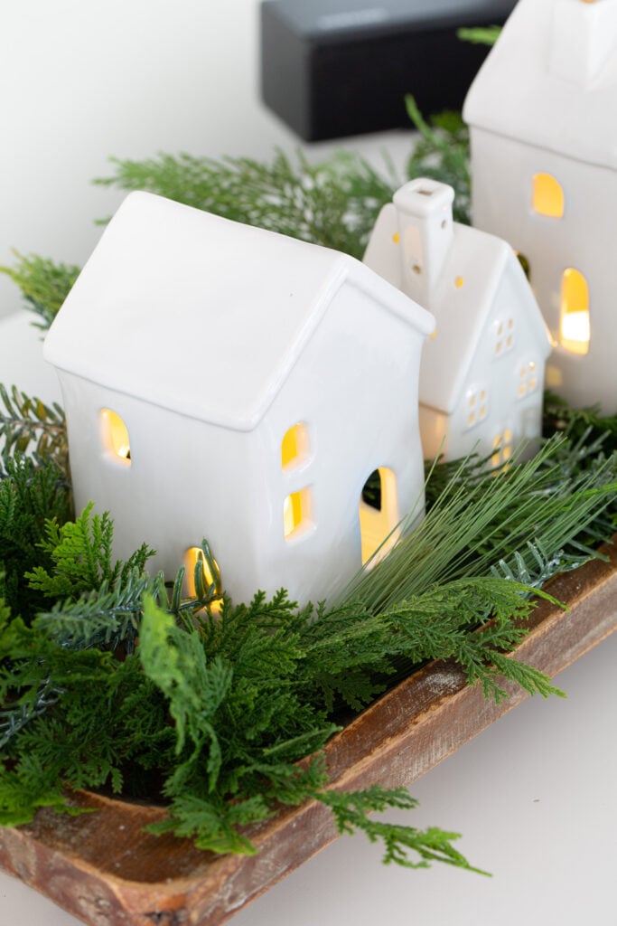 Christmas tabletop display using white ceramic houses lined up in a dough bowl with greenery around them.