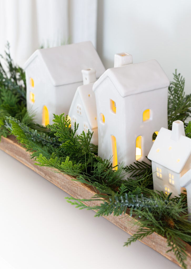 Christmas tabletop display using white ceramic houses lined up in a dough bowl with greenery around them.