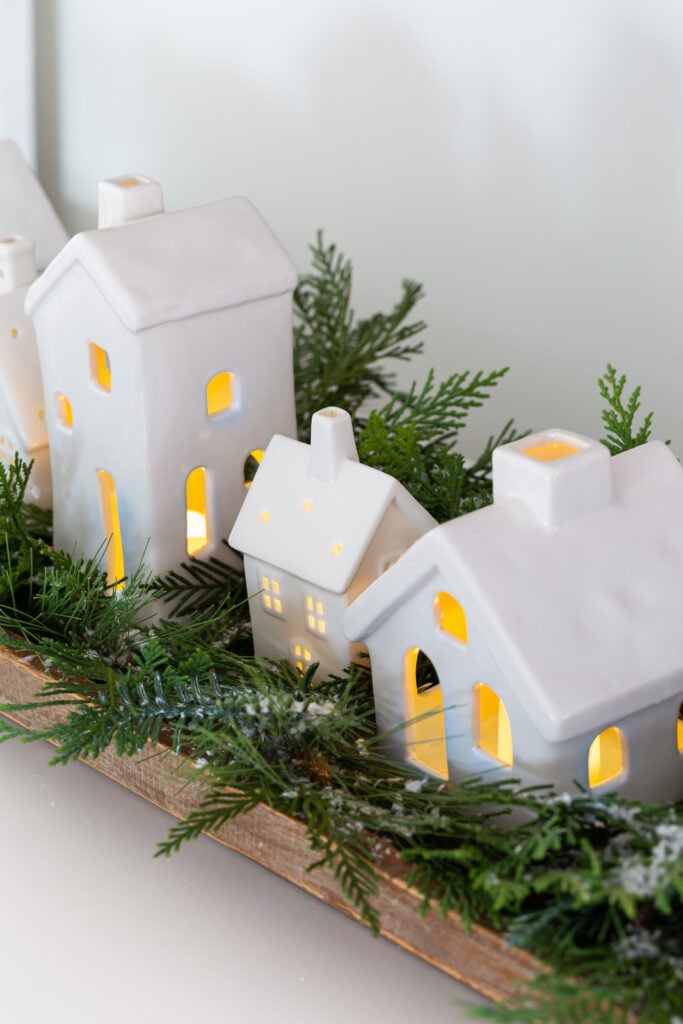 Christmas tabletop display using white ceramic houses lined up in a dough bowl with greenery around them.