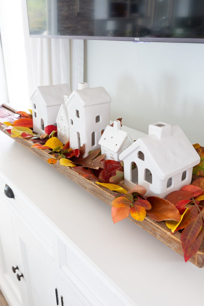 Ceramic Christmas village used with colorful fall leaves to be used for autumn decor in a home.