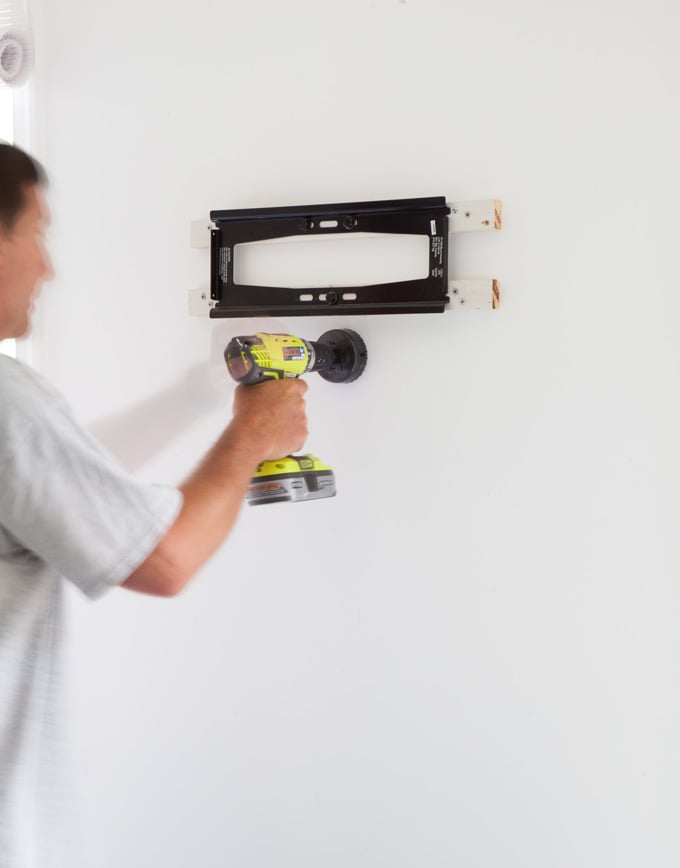 Man drilling hole in wall for TV cord kit to go into.