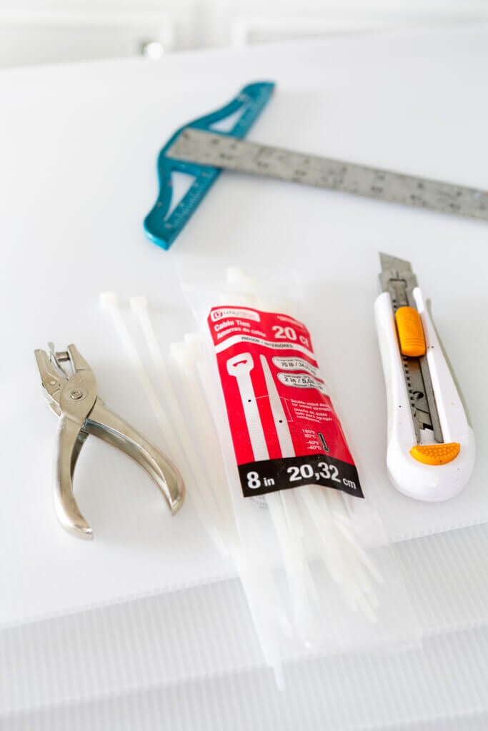 a paper hole punch, zip ties, craft knife and t-square on a table.