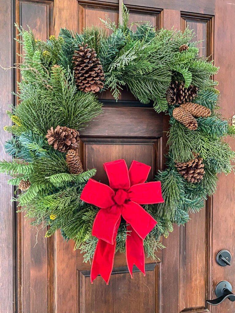 Evergreen wreath on door with red velvet wired ribbon bow.