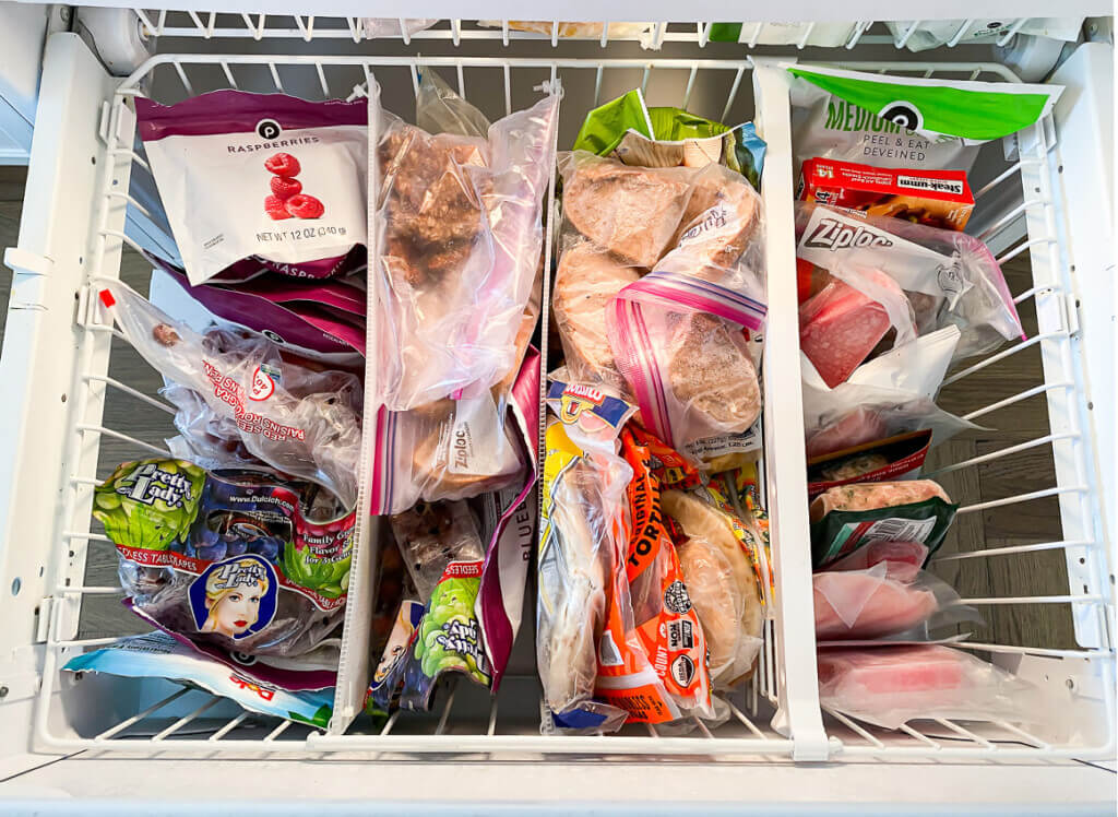 Looking down into a newly organized bottom drawer of a freezer filled with frozen food.