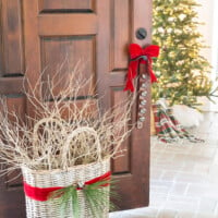 Red ribbon around large basket filled with branches. Christmas tree in distance.