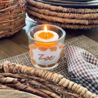 Burnt orange color votive candle in glass holder with free printable Thanksgiving place card hot glued to it.