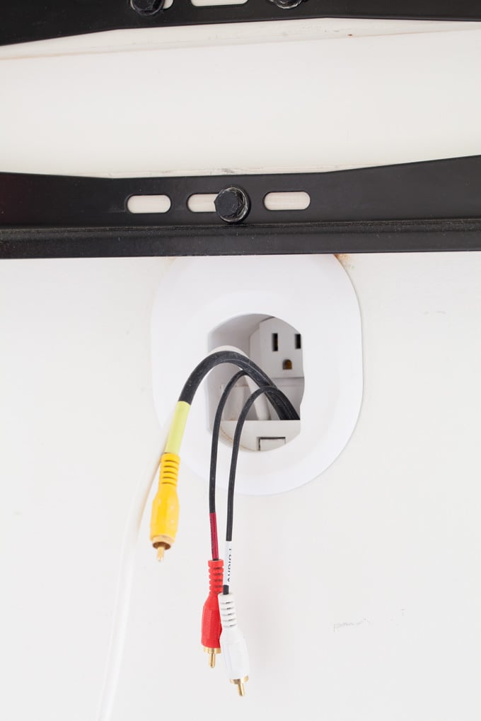 Wall-mounted-TV-cord-hiding-how-to-tutorial showing red and yellow cable wires coming out of wall under a TV wall mounting bracket.