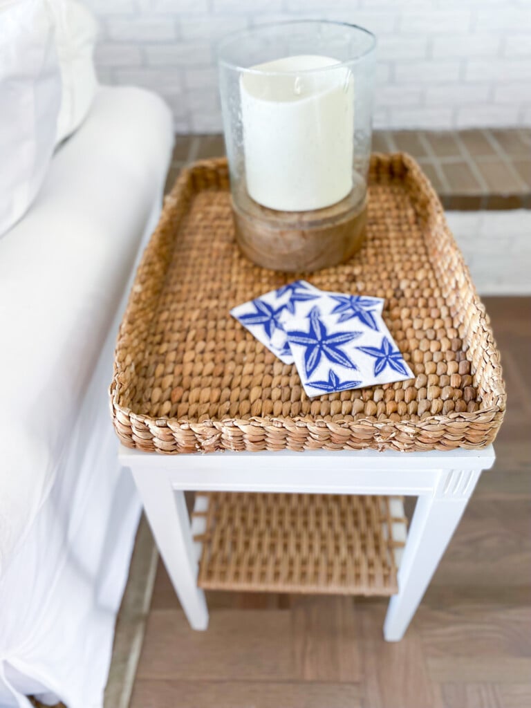 looking down at the top of a coastal inspired painted side table with a woven rattan style bottom shelf.